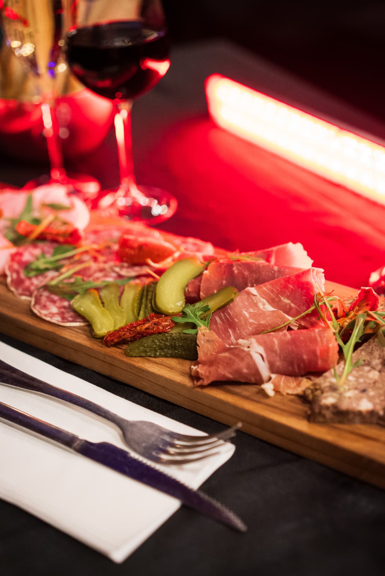 Planche de charcuterie italienne et cornichons sous une lumière rouge