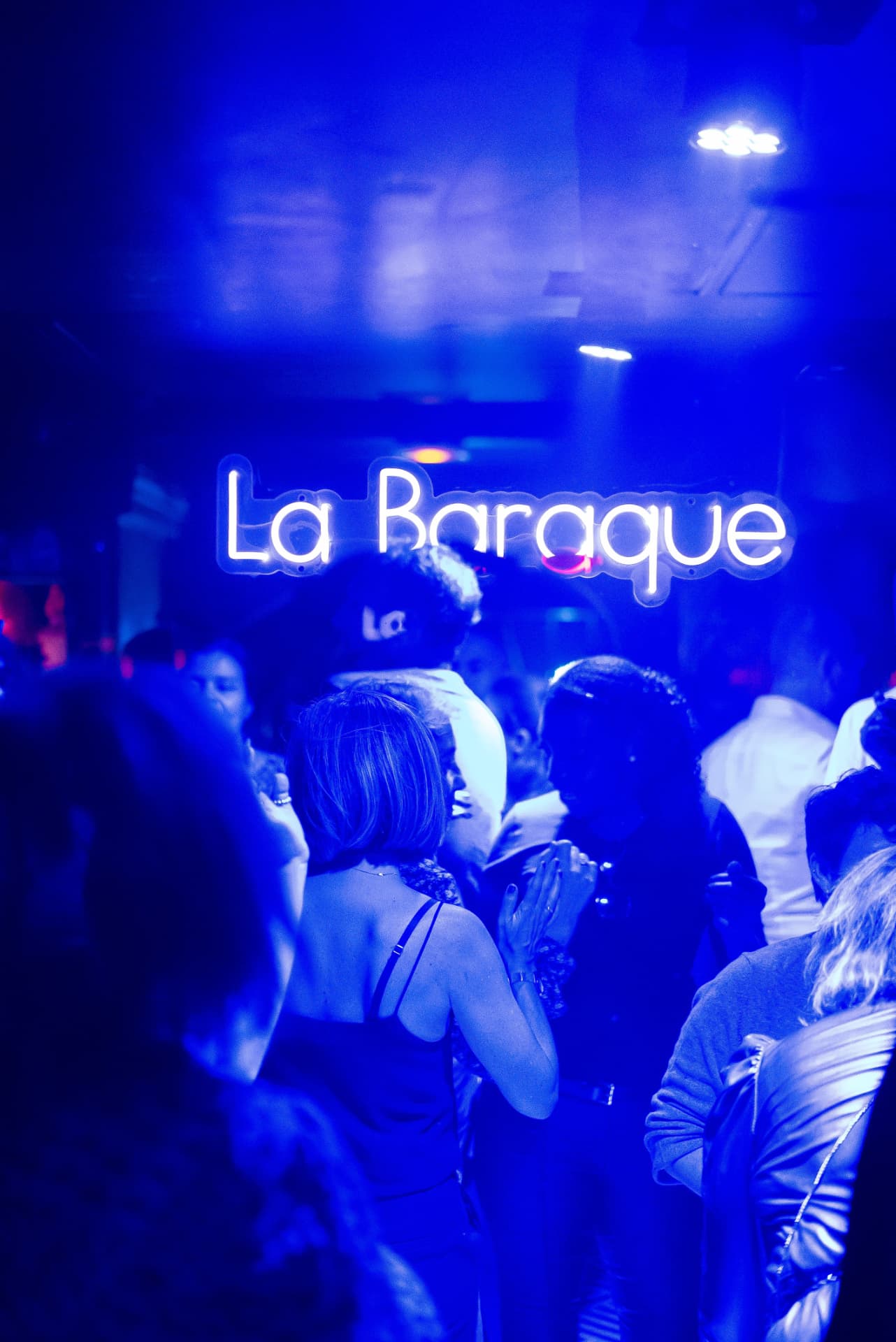 Enseigne néon La Baraque au-dessus de la foule dans une lumière bleue