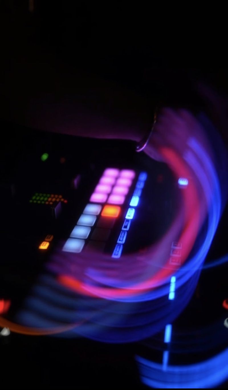 Main du DJ sur la console de mixage aux pads lumineux, traînées de lumière bleue et rose à La Baraque