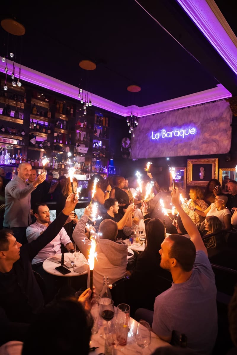 Long table of guests raising sparkler fountains under the La Baraque sign